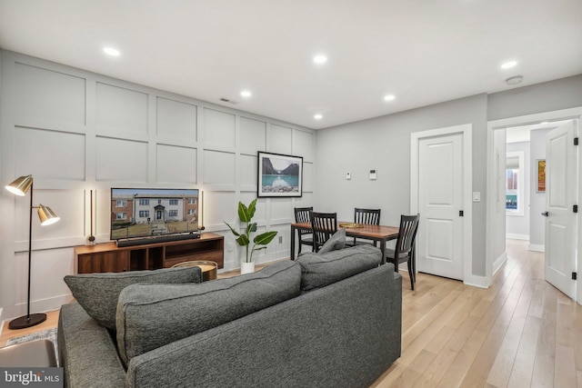 living room with light wood finished floors, visible vents, baseboards, a decorative wall, and recessed lighting