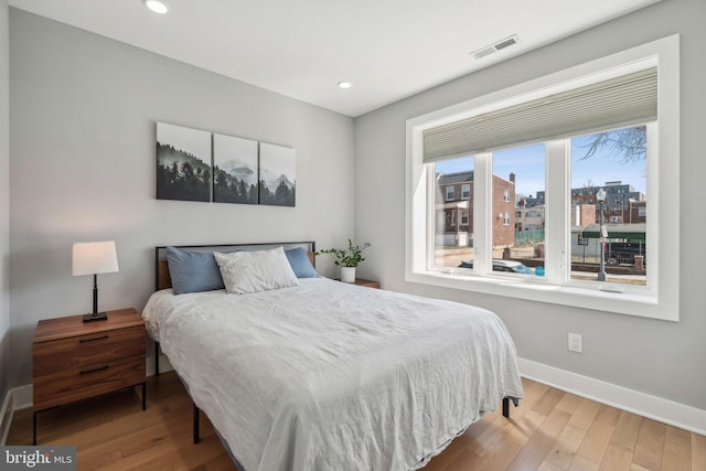 bedroom with a view of city, recessed lighting, visible vents, wood finished floors, and baseboards