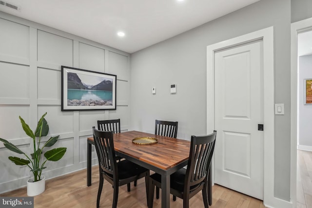 dining area with light wood-type flooring, visible vents, a decorative wall, and recessed lighting