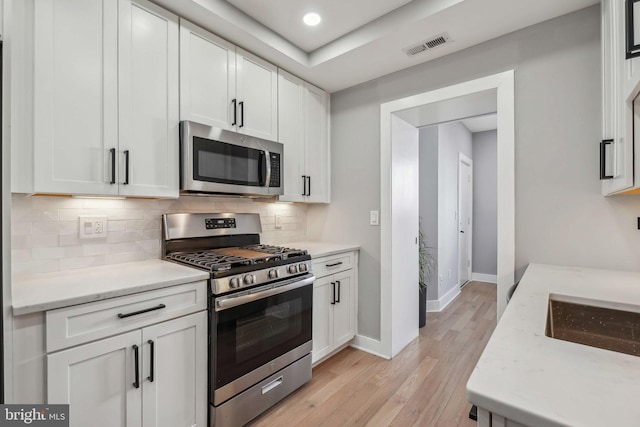 kitchen with stainless steel appliances, white cabinetry, visible vents, light wood-type flooring, and decorative backsplash