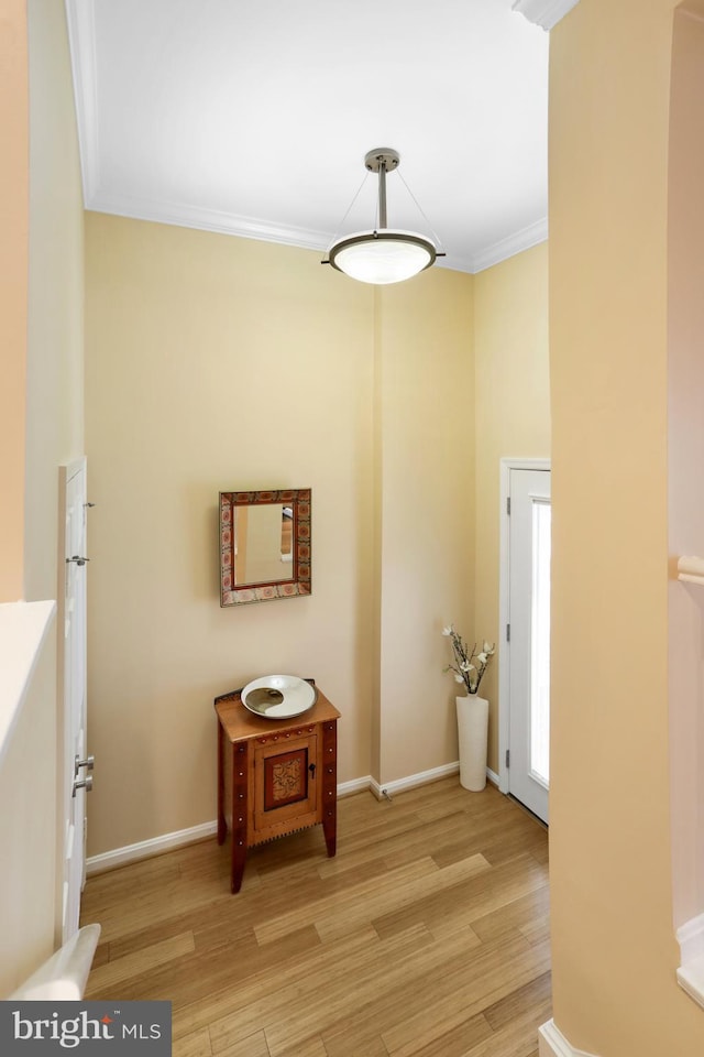 hall with light wood-style flooring, baseboards, and ornamental molding