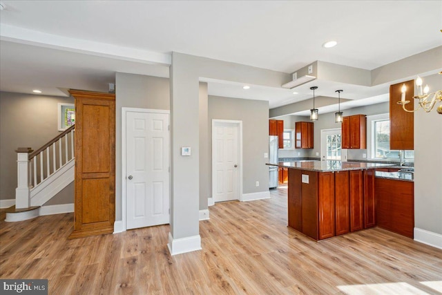 kitchen with a peninsula, baseboards, light wood-style floors, freestanding refrigerator, and brown cabinetry