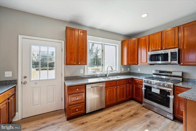 kitchen featuring appliances with stainless steel finishes, a healthy amount of sunlight, a sink, and light wood-style flooring