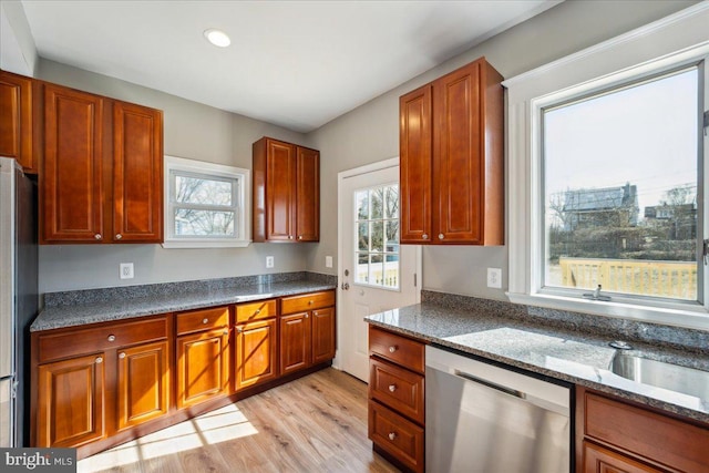 kitchen featuring light wood-style floors, appliances with stainless steel finishes, brown cabinets, and dark stone countertops