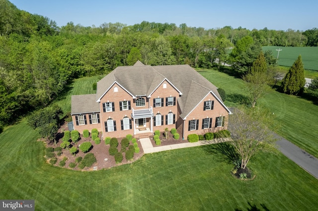 view of front facade featuring a balcony, a front lawn, a view of trees, and brick siding