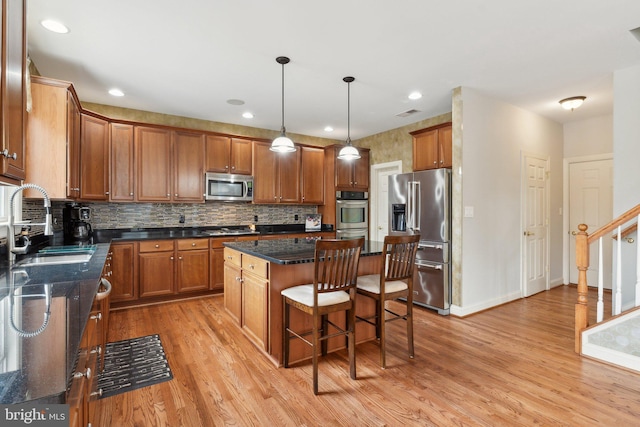 kitchen featuring a sink, a kitchen island, stainless steel appliances, brown cabinetry, and light wood finished floors