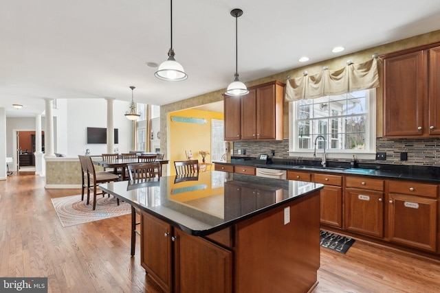 kitchen with light wood finished floors, dishwasher, dark countertops, and ornate columns