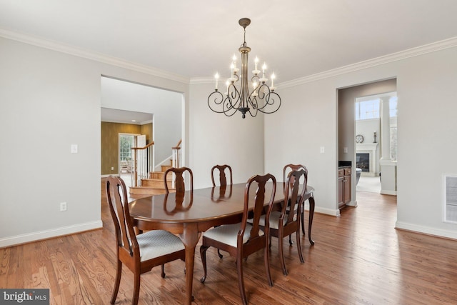 dining space with stairway, wood finished floors, baseboards, an inviting chandelier, and crown molding