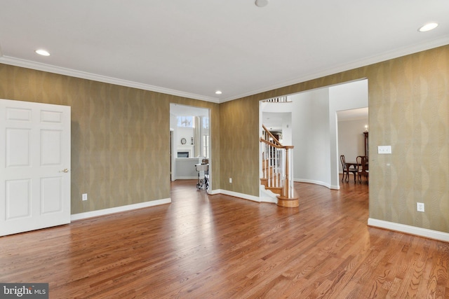 empty room featuring baseboards, wood finished floors, stairs, and crown molding