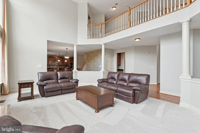 carpeted living area featuring a towering ceiling, baseboards, and decorative columns