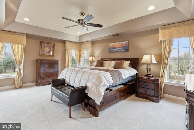 bedroom featuring visible vents, light colored carpet, a raised ceiling, and multiple windows