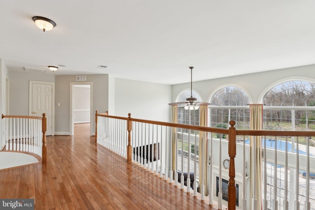 corridor with hardwood / wood-style flooring, an upstairs landing, visible vents, and baseboards