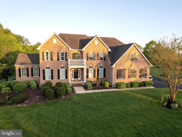 colonial house with brick siding, a balcony, and a front lawn