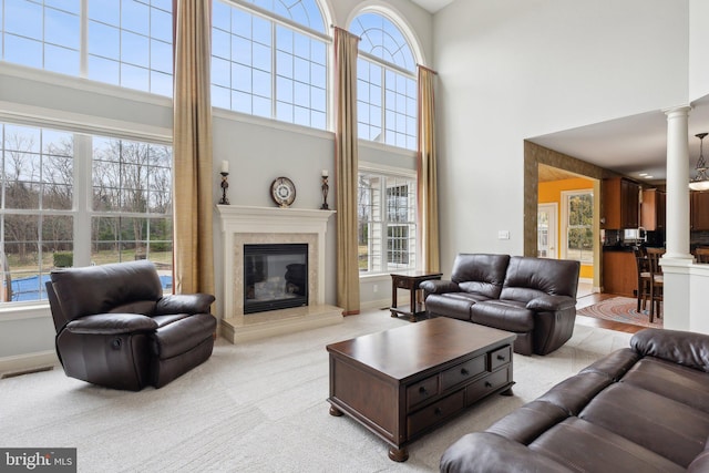 living area with visible vents, baseboards, light carpet, a fireplace, and ornate columns