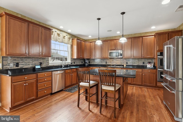 kitchen featuring a center island, a kitchen bar, brown cabinets, appliances with stainless steel finishes, and light wood-style floors