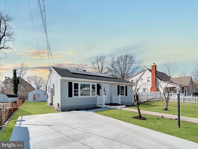 view of front facade featuring a shingled roof, fence, a front lawn, and solar panels