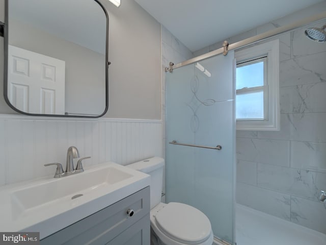 bathroom with toilet, a shower stall, vanity, and wainscoting