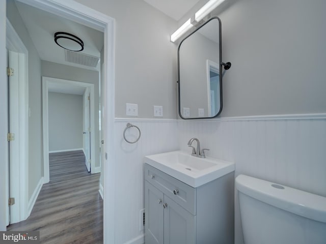 bathroom with a wainscoted wall, vanity, toilet, and wood finished floors