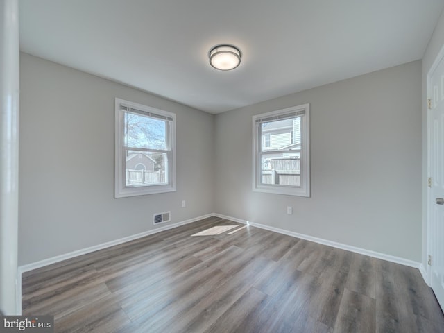 unfurnished room with wood finished floors, visible vents, and baseboards