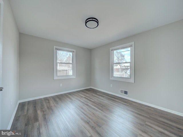 empty room with baseboards, visible vents, and wood finished floors