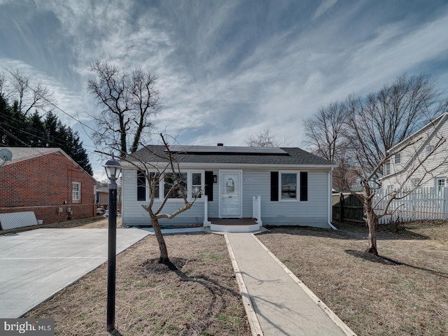 view of front of house featuring solar panels, concrete driveway, fence, and a front yard