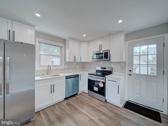 kitchen featuring white cabinets, light wood-style flooring, appliances with stainless steel finishes, a sink, and backsplash