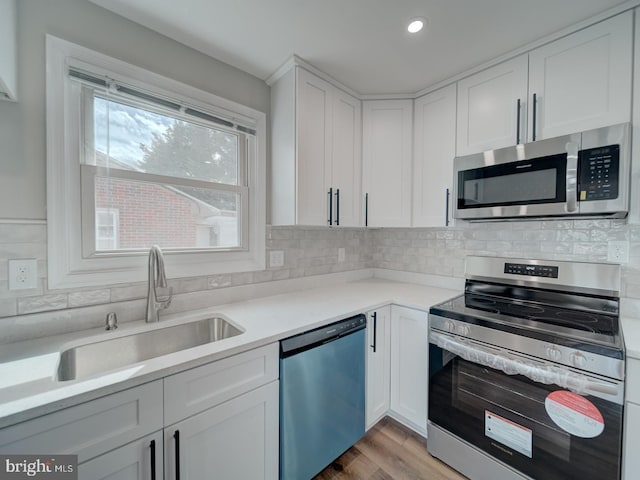 kitchen with stainless steel appliances, a sink, white cabinets, light countertops, and backsplash