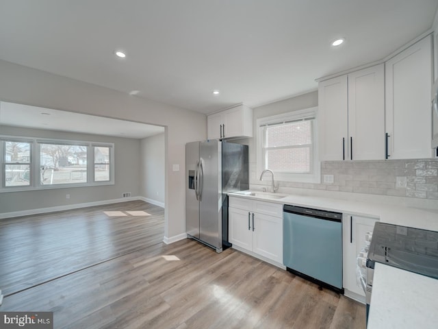 kitchen with stainless steel appliances, tasteful backsplash, a sink, and light wood-style flooring