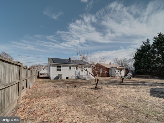 rear view of house with a fenced backyard and roof mounted solar panels