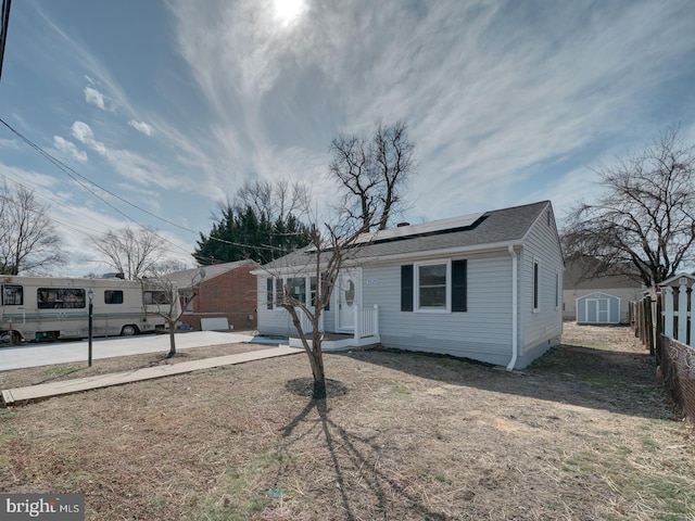 view of front of property featuring a shingled roof, a storage shed, roof mounted solar panels, fence, and an outdoor structure