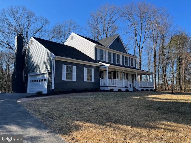 colonial-style house with driveway, an attached garage, a chimney, and a porch