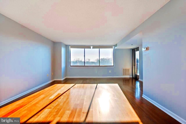 empty room featuring baseboards, visible vents, and dark wood finished floors