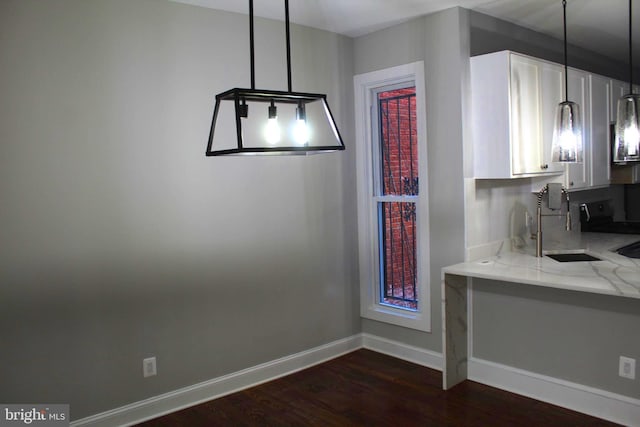 unfurnished dining area with dark wood-style flooring, a sink, and baseboards
