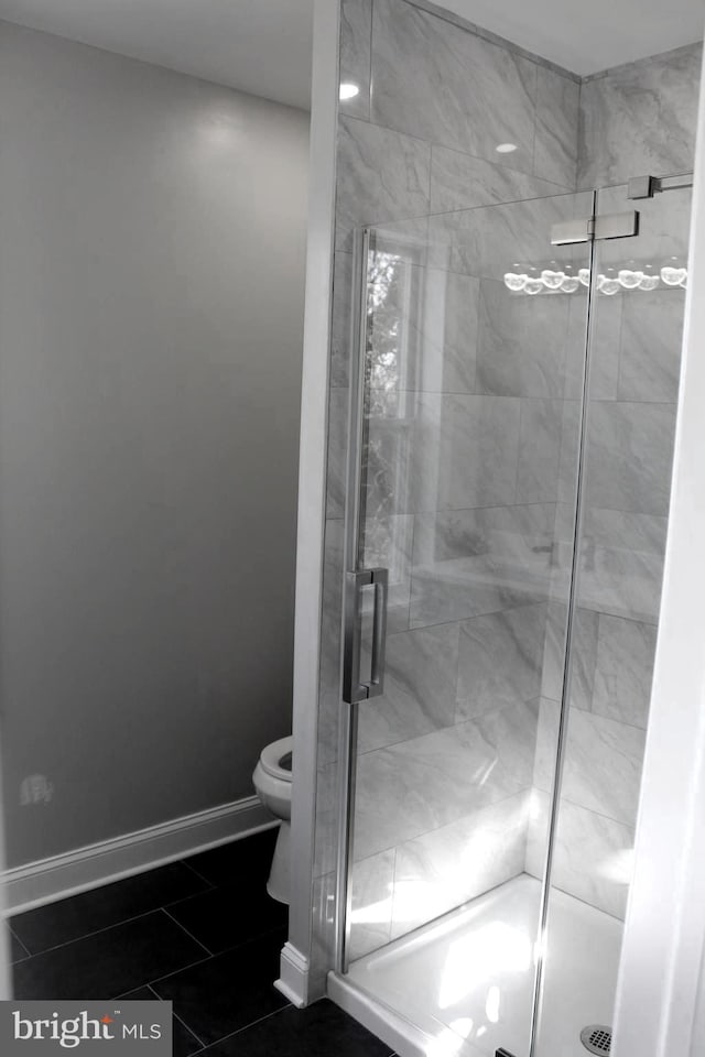 bathroom with toilet, a shower stall, and baseboards