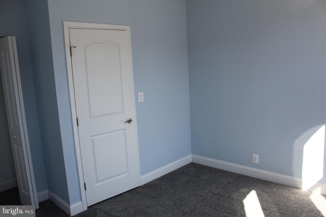 unfurnished room featuring baseboards and dark carpet