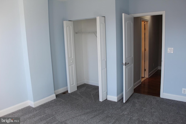 unfurnished bedroom with dark colored carpet, a closet, and baseboards