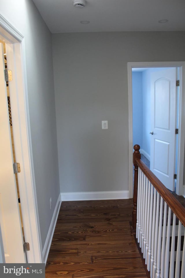 corridor featuring baseboards, dark wood-type flooring, and an upstairs landing