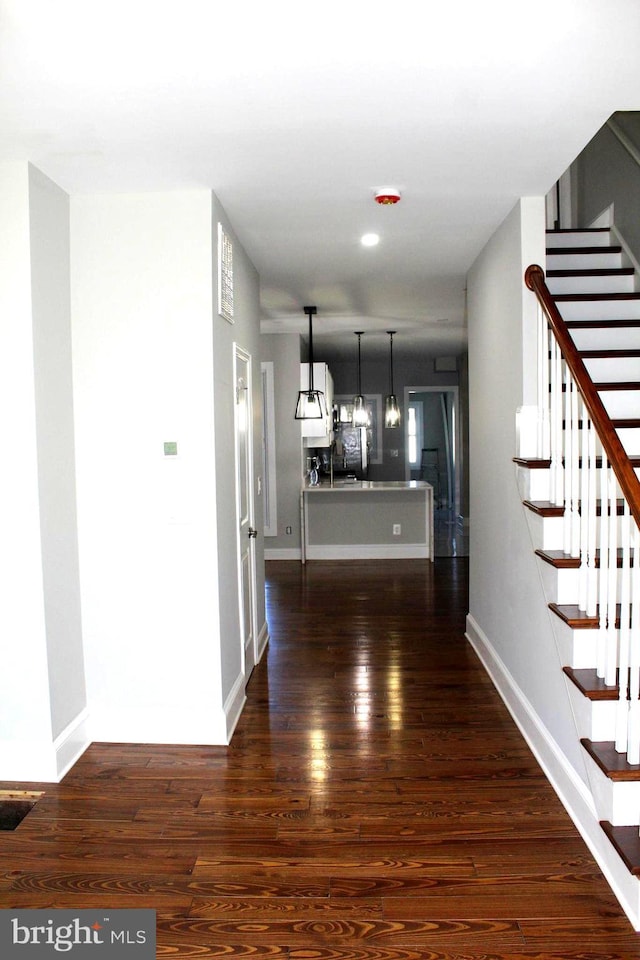 corridor featuring dark wood-style floors, baseboards, and stairs