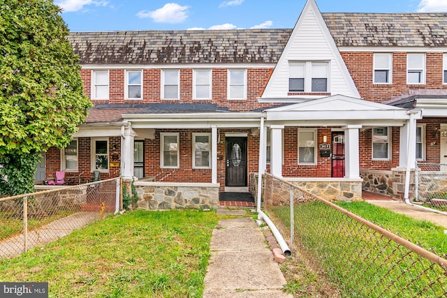 multi unit property featuring covered porch, a fenced front yard, a front yard, and brick siding