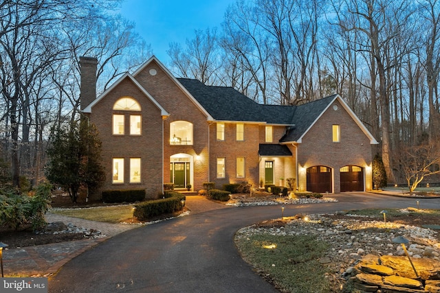 view of front facade with brick siding, driveway, and a chimney