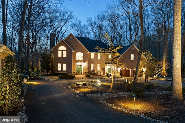 view of front facade with brick siding, a chimney, and curved driveway