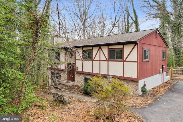 view of side of home with stone siding, roof with shingles, and fence