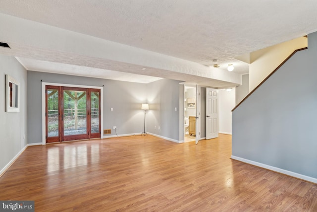 unfurnished living room featuring a textured ceiling, light wood-style flooring, and baseboards