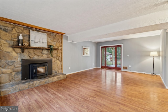 unfurnished living room with a wood stove, a textured ceiling, baseboards, and wood finished floors