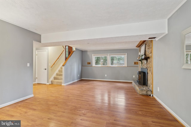 unfurnished living room featuring a fireplace, stairway, light wood finished floors, and a textured ceiling