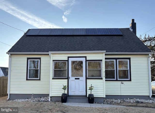 view of front of home with a shingled roof, a chimney, and solar panels