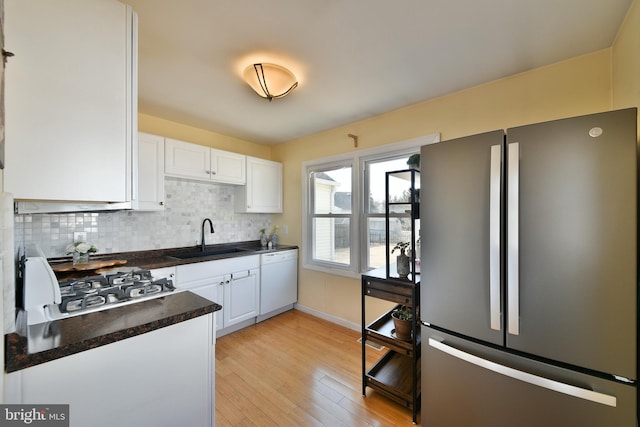 kitchen with white dishwasher, a sink, white cabinetry, freestanding refrigerator, and dark countertops