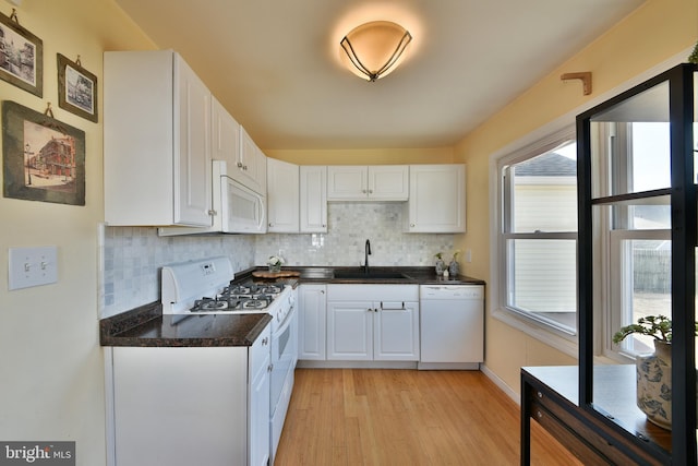 kitchen with dark countertops, white appliances, white cabinets, and a sink