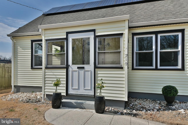 doorway to property with roof mounted solar panels and roof with shingles