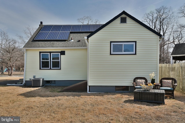 back of property with roof with shingles, a yard, roof mounted solar panels, central AC, and fence